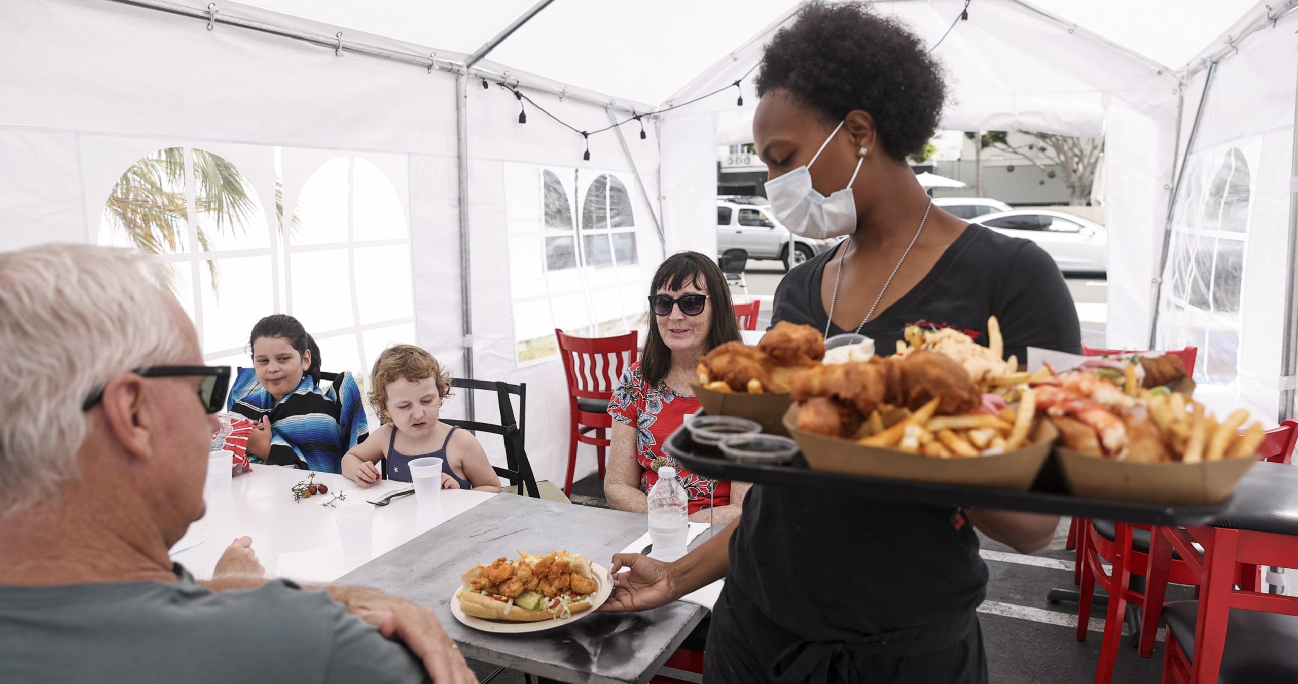 Young Waitress Serving Food to Customers in Outdoor Tent Wearing a Mask